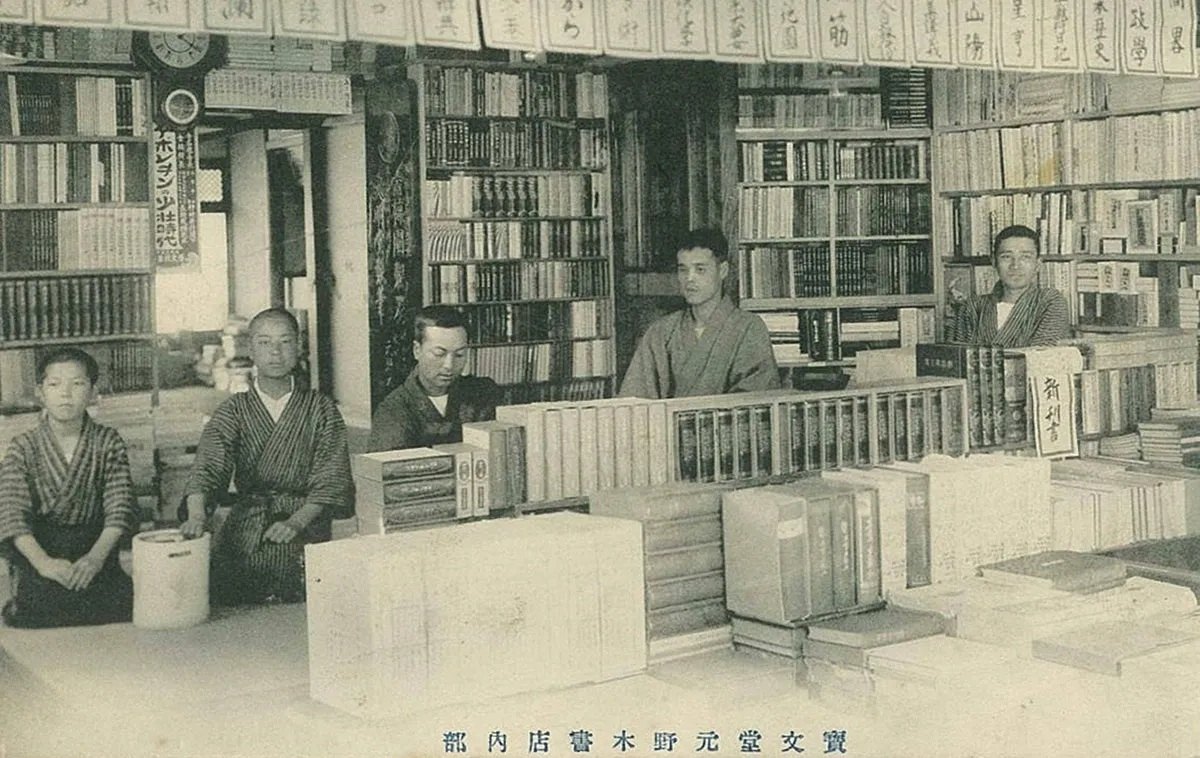 大正五年の店内。壁一面の本棚と、台の上に積まれた本の前に、着物姿の男性と少年の合わせて五人が並んでいる古い白黒写真。